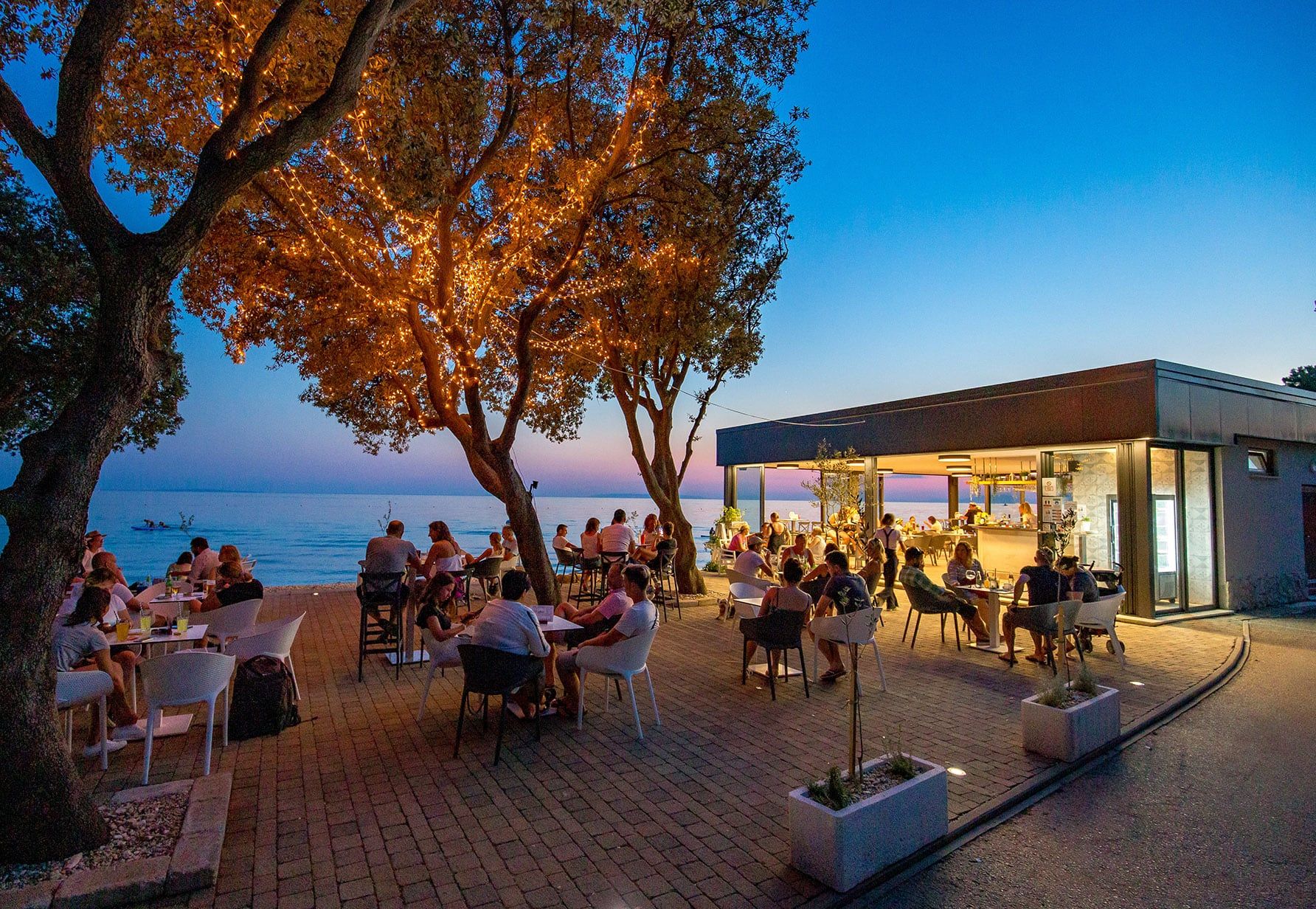 Beach bar uz more u suton, gosti za stolovima