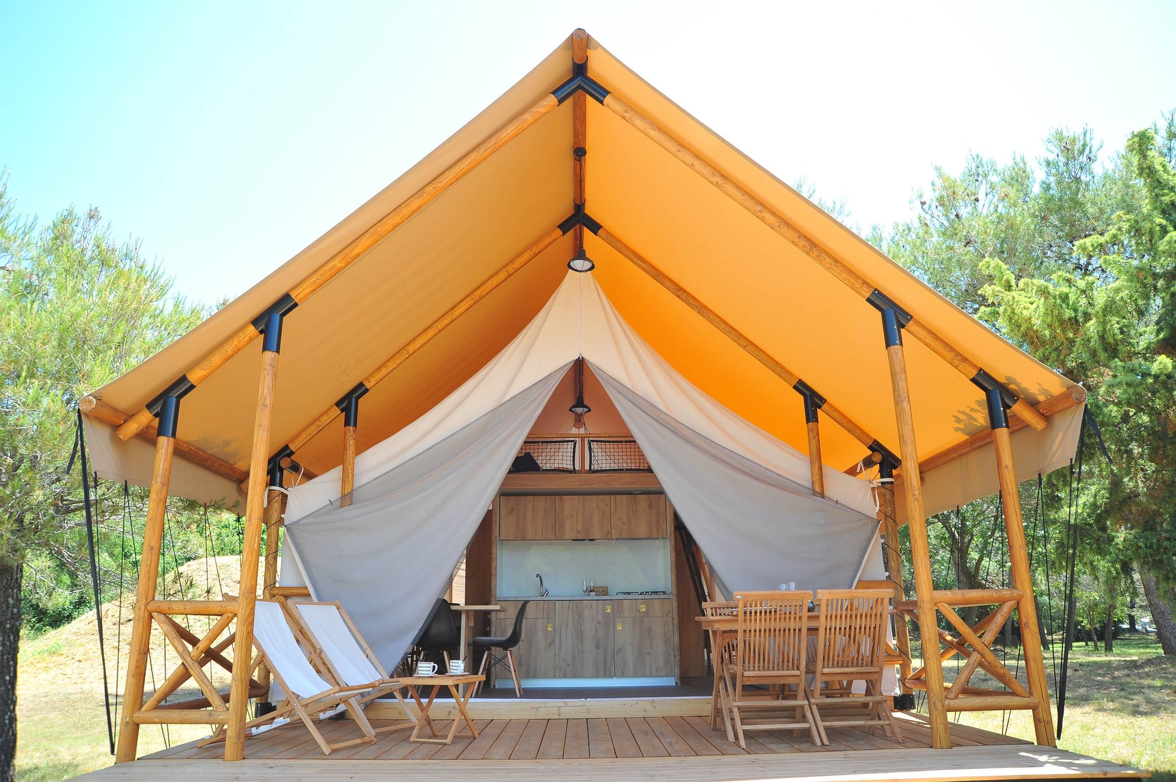 Glamping šator s drvenom terasom, ljuljačkom i ležaljkama među stablima