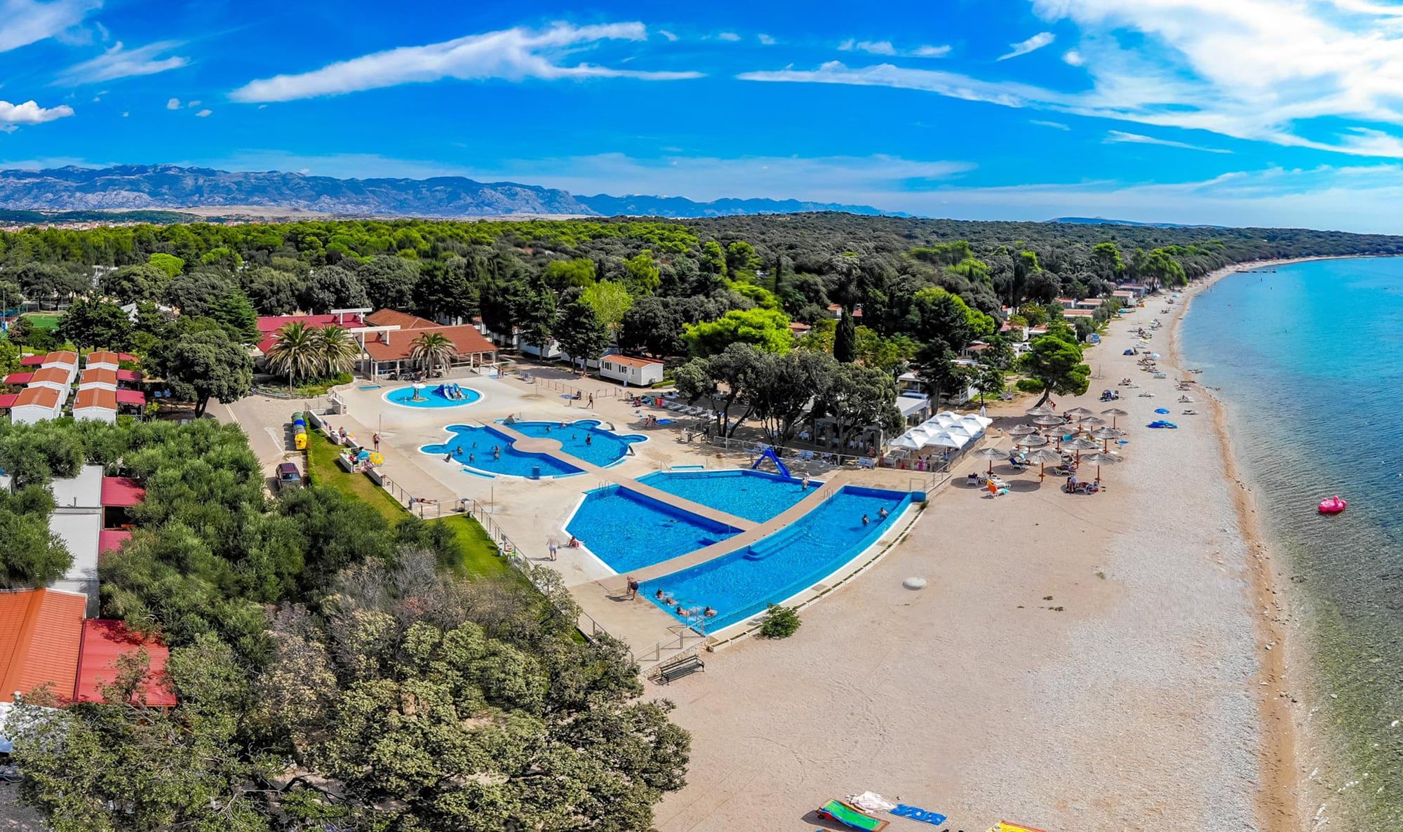 Kamp Straško iz zraka: bazeni, duga plaža i hrastova šuma, a u daljini Velebit