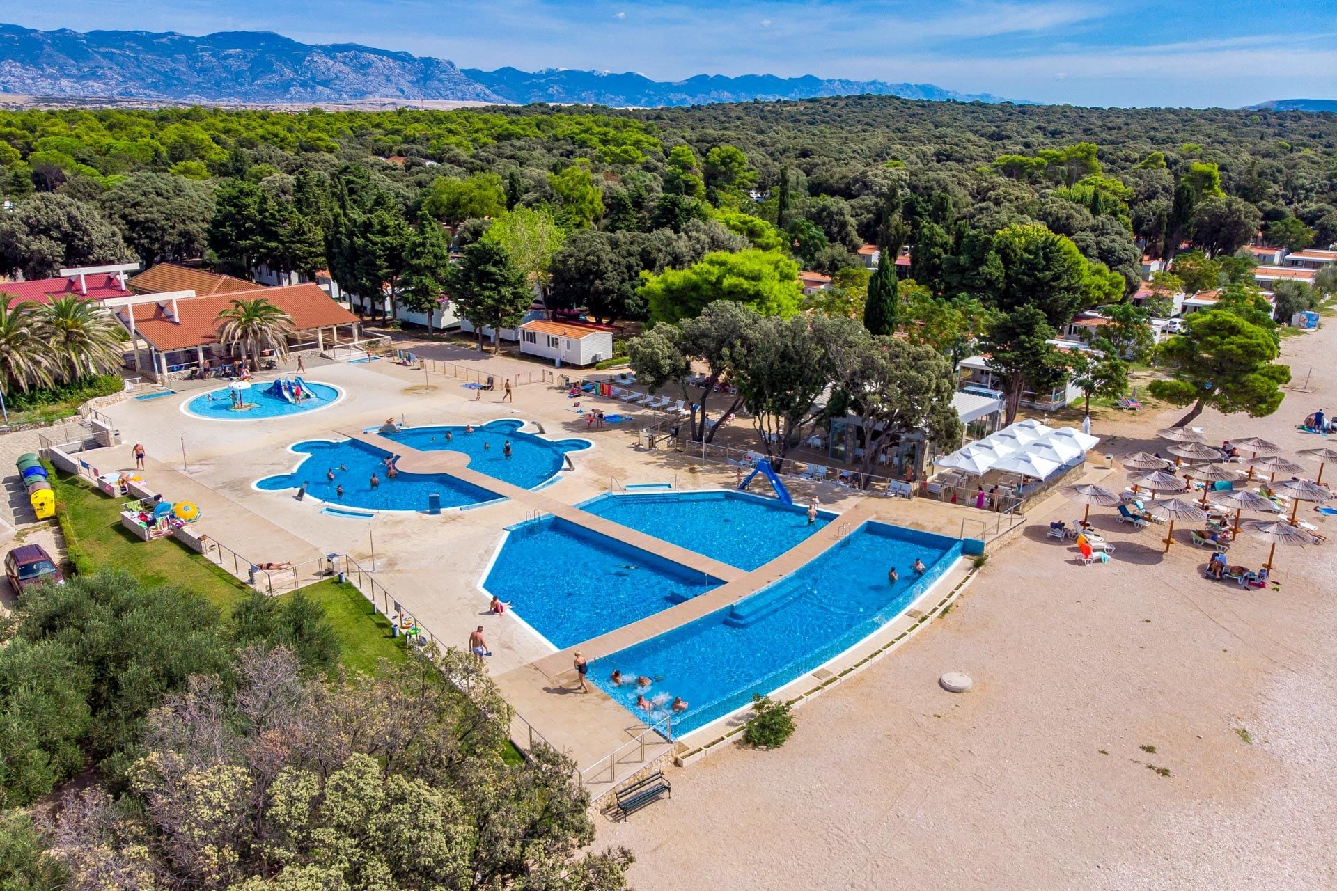 Kamp Straško iz zraka: bazeni, plaža i šuma, a u daljini Velebit